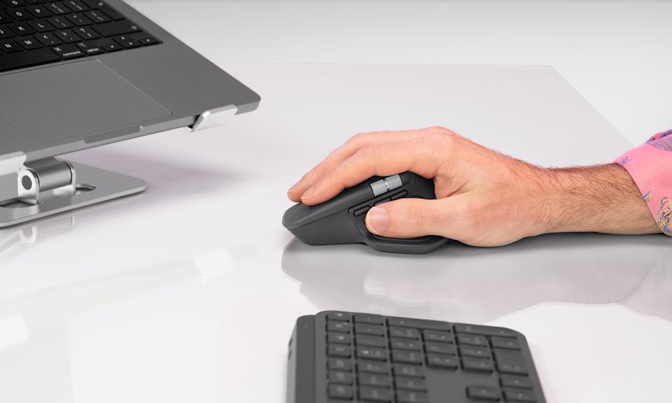 A man uses a graphite Logitech MX Master 4 wireless mouse on a white glossy desk.