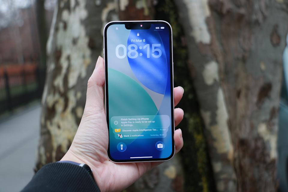 An iPhone 17e held up in front of a tree trunk.