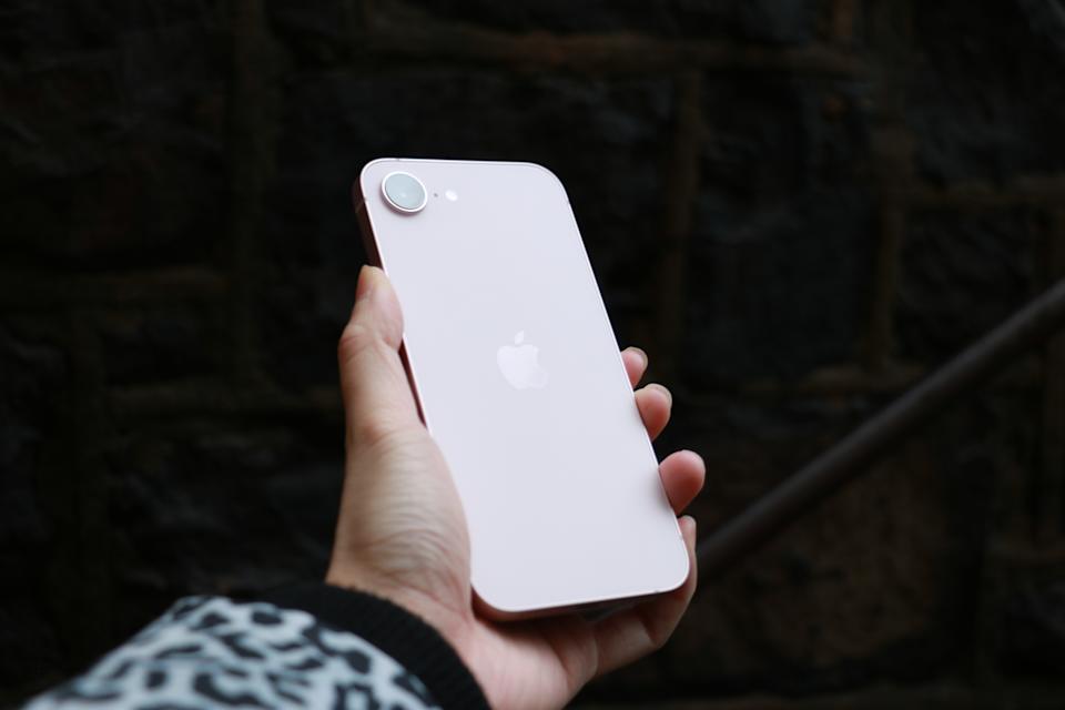 The rear of the iPhone 17e catches the light in front of a stone wall.
