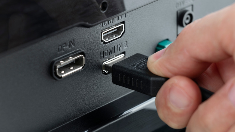 A hand plugs an HDMI cable into the HDMI input on the back of a monitor.