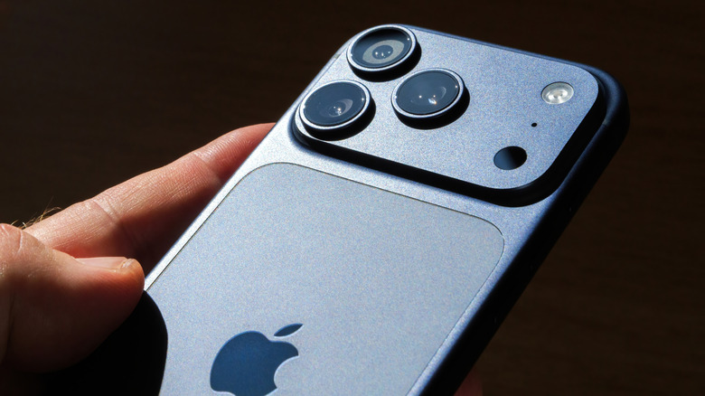 A hand holds up the back of a sleek iPhone against a dark background.