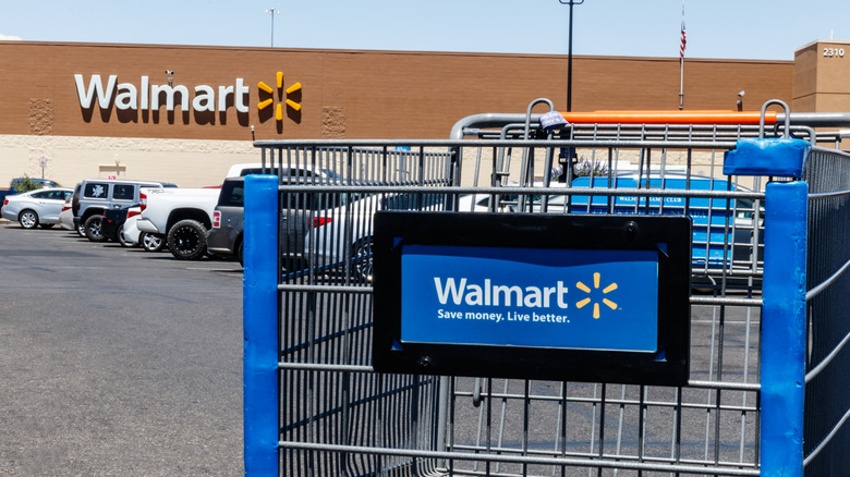 A Walmart shopping cart sits front and center in a crowded store parking lot.