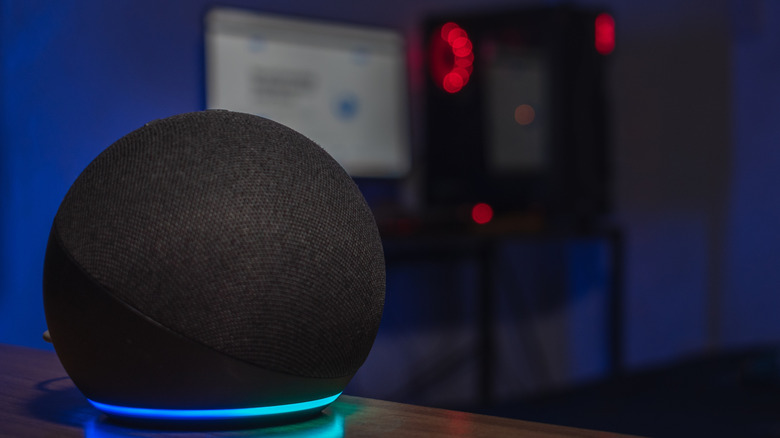 Dark room picture of an Amazon Echo, a blurry computer screen and tower in the background.