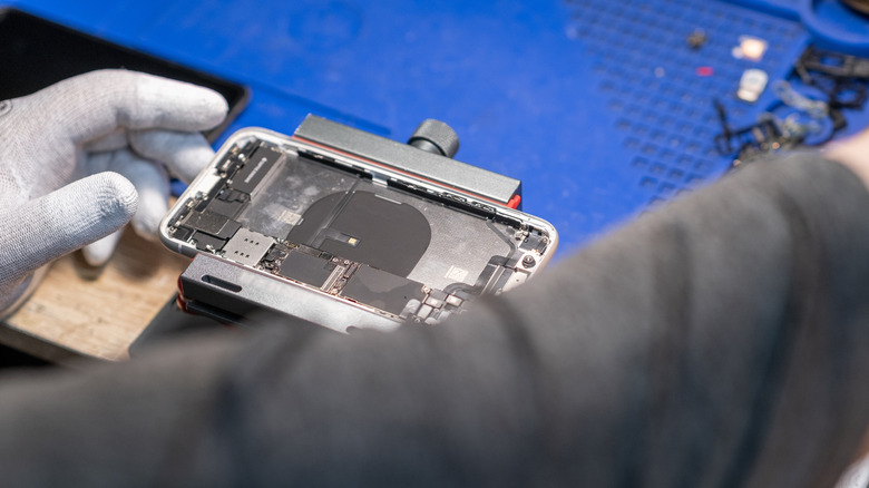 Technician inspecting and repairing a smartphone at a workbench.