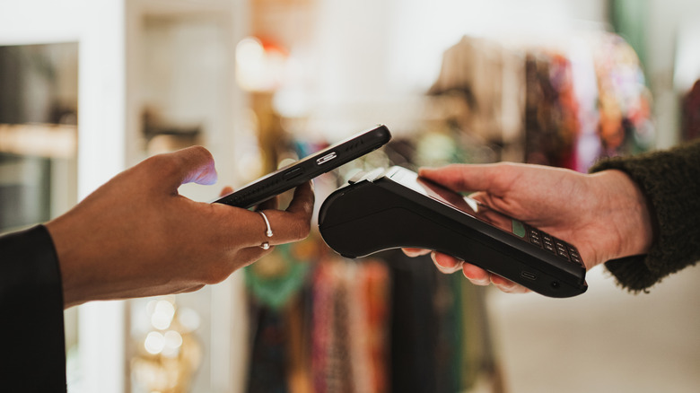 A smartphone being used to make a payment using tap-to-pay against a portable contactless terminal.