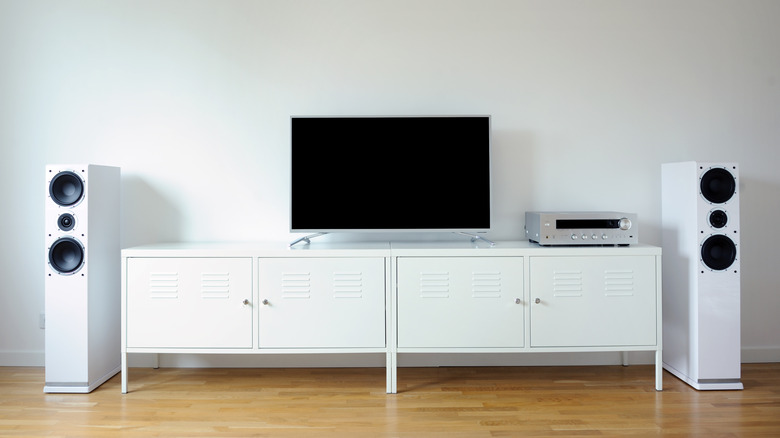 White entertainment center with a TV on top, directly centered, flanked by two tall, white speakers.