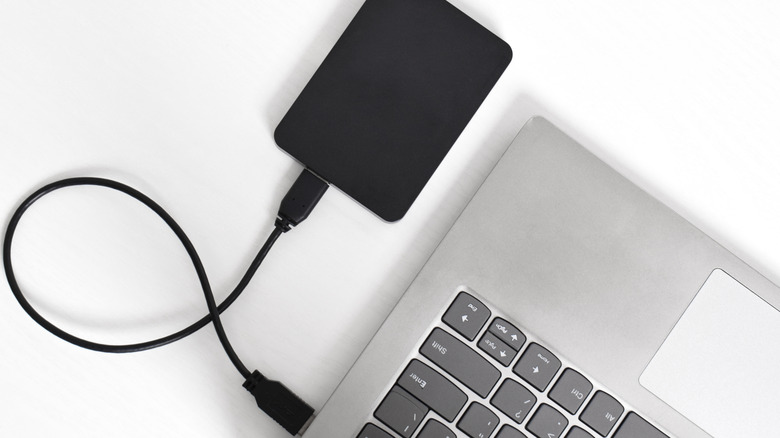 A black external hard drive plugged in to a silver laptop.
