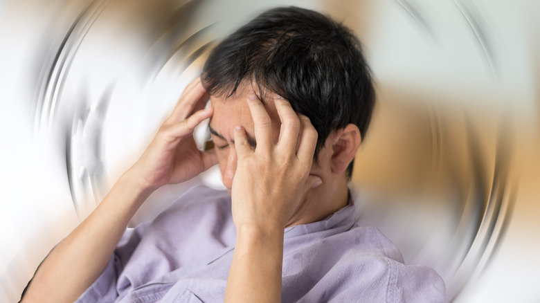 A man holds his head in his hands in front of a blurred, swirling background.