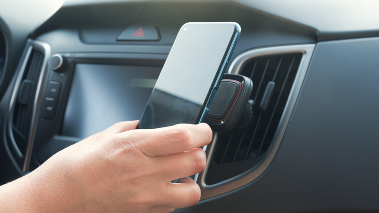 Hand placing a smartphone into a car air vent mount.