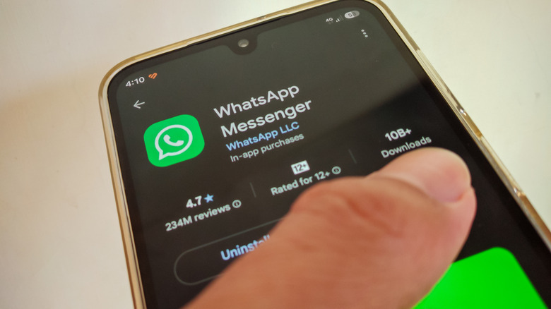 A thumb tapping on the screen of an Android phone showing WhatsApp on the Google Play Store.
