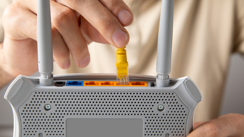 Hand holding a router and plugging a yellow Ethernet cable into it.