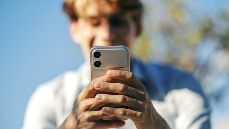 A man out of focus smiles while using his iPhone