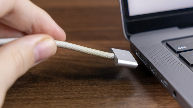Unplugging a MagSafe charging cable from a MacBook.